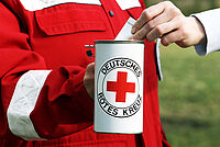 Rotkreuzmitglied mit roter Einsatzjacke wirbt mit Spendendose um Spenden
